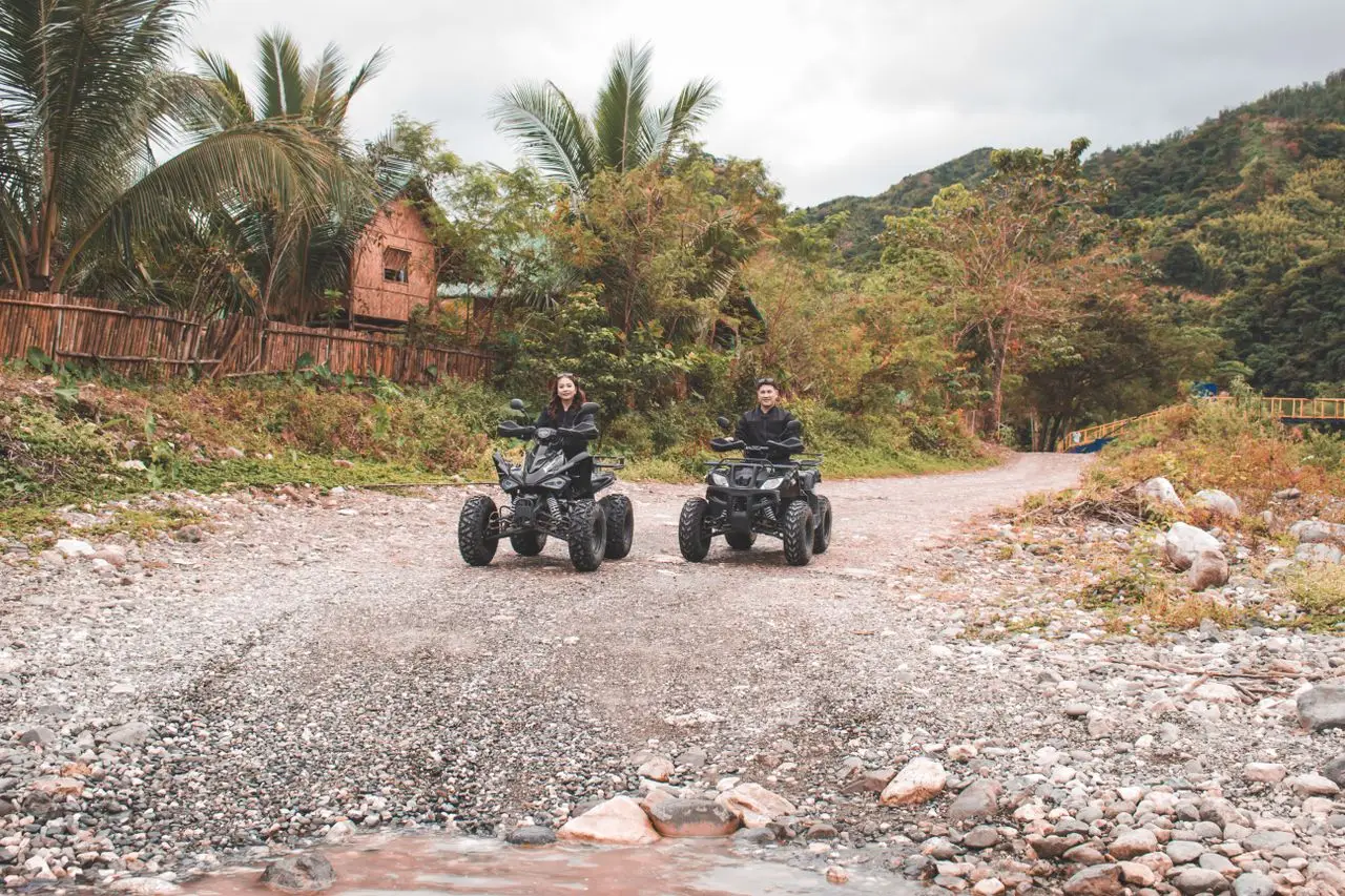A couple enjoying a rural adventure riding quad bikes on a scenic gravel road.